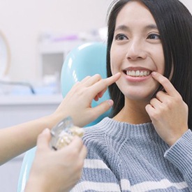 Patient pointing to her smile as dentist examines her teeth