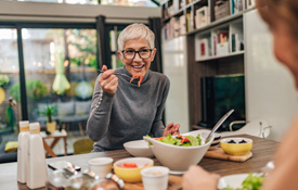 Woman with black glasses smiling while eating with friend
