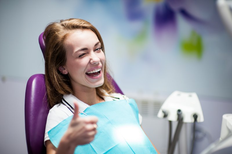 Woman with no cavities giving thumbs up at the dentist